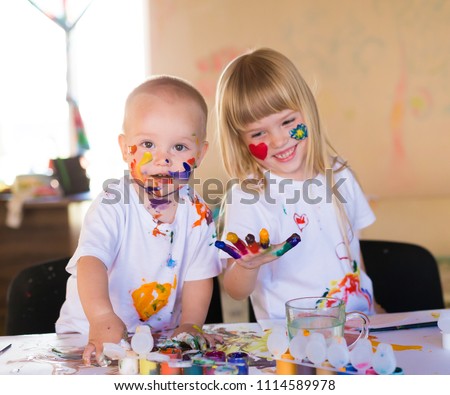 Beautiful little blonde girl and boy, has happy fun smiling face, brown eyes, white t-shirt. Painted brushes water colors in skin. Child portrait. Kids concept. Brother and sister hobby.