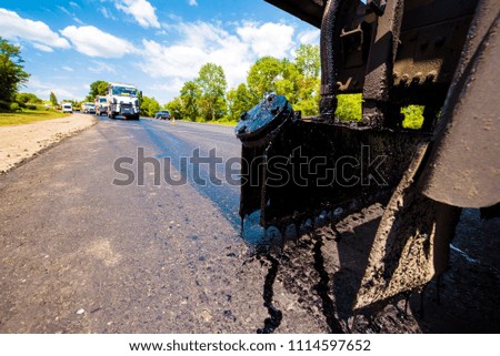  fragment of a truck mechanism with a flowing resin during road repair on the background of trucks with asphalt