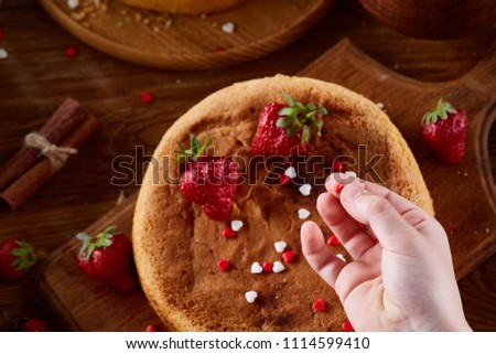 Close up of girl's hands decorating top of delicious strawberry cake, close up, selective focus.