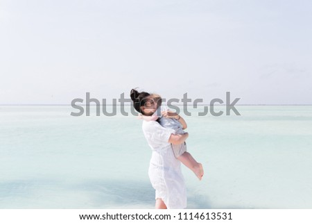 Happy family embracing at beach in summer near blue sea. Mother and toddler boy hugging and kissing together
