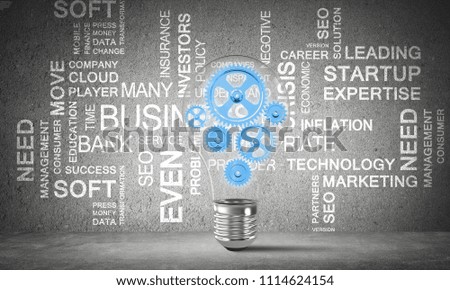 Glass lightbulb with multiple gears inside placed against business related terms on grey wall on background. 3D rendering.