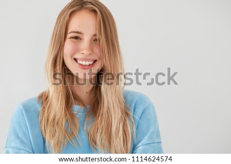 Studio shot of happy Caucasian female has broad smile, shows white teeth, being in high spirit after celebrating friend`s birthday, enjoys recreation time in merry company, isolated over white wall