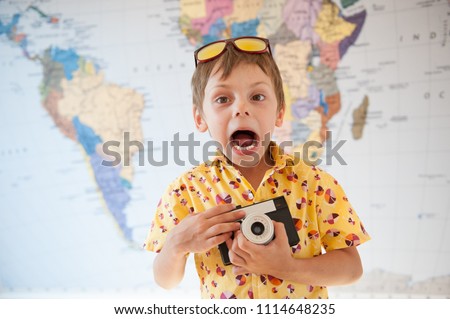 funny shouting little kid in yellow shirt with vintage camera in hands on world map backdrop