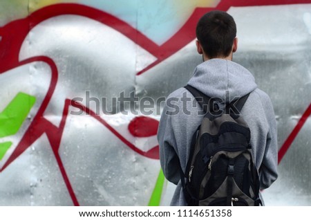 A young graffiti artist with a black bag looks at the wall with his graffiti on a wall. Street art concept