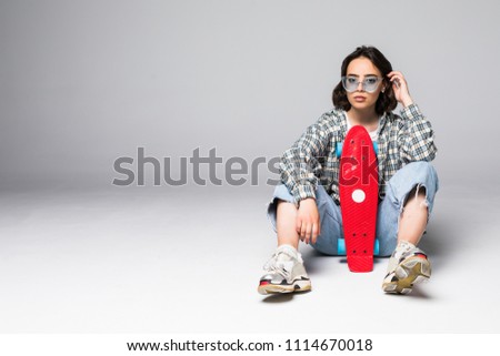 Happy young woman in sunglasses sitting on skateboard over gray background