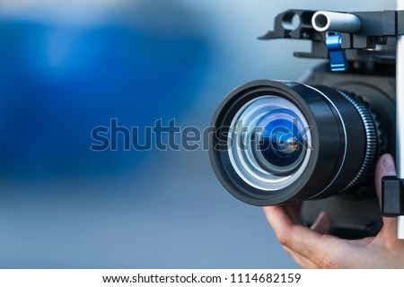 Camera lens attached to a camera and hand focusing close up detailed with smooth blue background and sunset reflections. Concept for videography cinematography vlogging video television movies making  Royalty-Free Stock Photo #1114682159