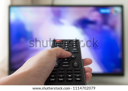 Close up Hand holding TV remote control with a television in the background.