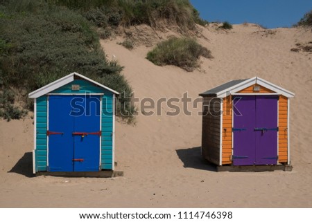 Brightly painted beach huts in a row on Saunton Sands, North Devon UK. backdrop of sand dunes and blue sky on a sunny summers day