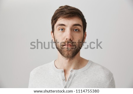 Keep calm and pretend nothing happened. Portrait of calm serious mature male with beard standing with no emotions over gray background, staring at camera without interest. Man careless about anything