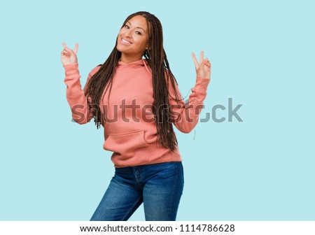 Portrait of a young black woman wearing braids fun and happy, positive and natural, makes a gesture of victory, peace concept