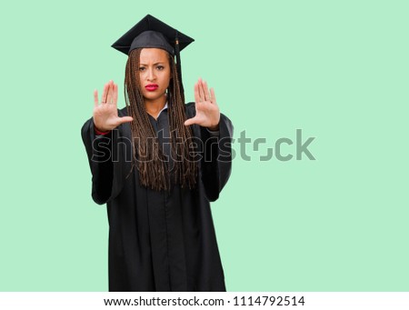Young graduated black woman wearing braids serious and determined, putting hand in front, stop gesture, deny concept