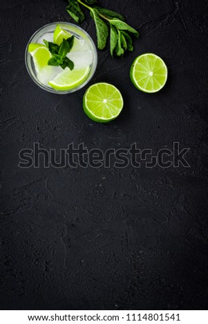 Tropical cocktail. Beverage which women likes. Glass of mojito with slices of lime, mint, ice cubes on black background top view copy space