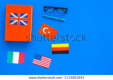 Language study concept. Textbooks or dictionaries of foreign language near flags on blue backgrond top view copy space