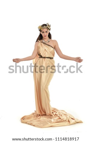 full length portrait of brunette girl wearing golden fantasy toga.   standing pose on white background.
