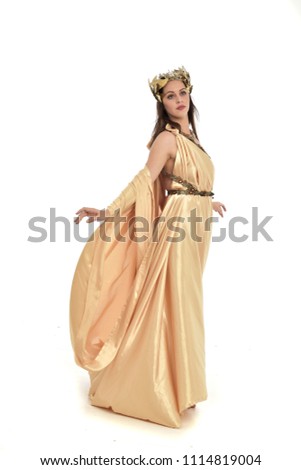 full length portrait of brunette girl wearing golden fantasy toga.   standing pose on white background.
