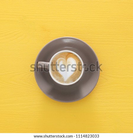 image of coffe cup with foam of heart shape over wooden yellow background