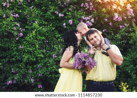 Happy family in park with blooming lilac. Mom, dad and son happy walk at sunset. Concept of happy family. Son sits on shoulders of pope.