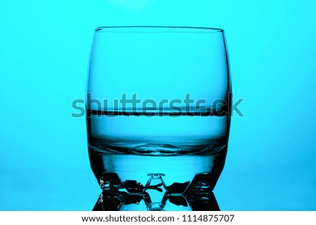 Clean drinking water in a round glass cup on blue background