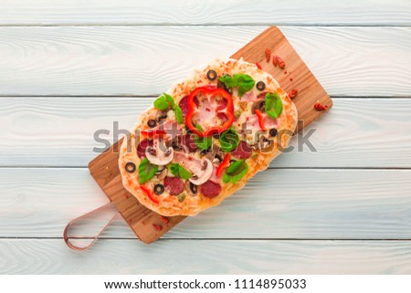 Homemade pizza with ham, pepperoni, mushrooms, capers and olives on a wooden table