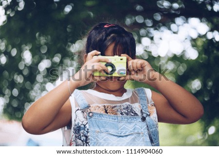 Little girl Asian takes photo with toy camera on nature green bokeh background