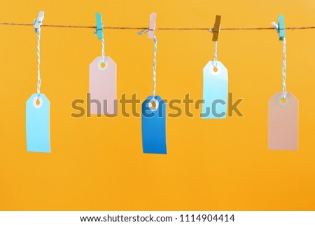 On a bright orange background photographed labels. Five multicolored empty labels hang on a rope pinned with clothespins. Bright layout, mock up.