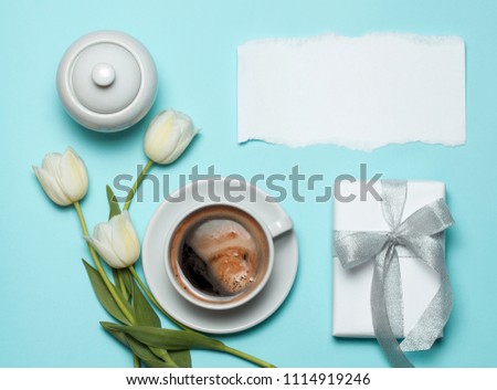 Cup of coffee and white tulips with gift box on blue background. Copyspace for text. spring coffee gift concept. top view, flat lay.
