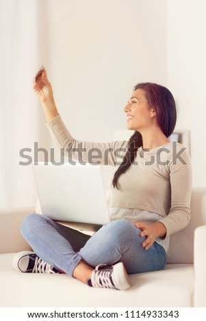 Portrait of young woman taking a self portrait with the smart phone on a couch at home 