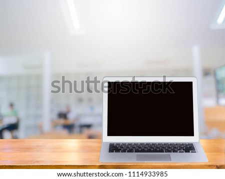 Laptop on wooden desk in library in college,blurred background.