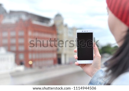 Close up image of woman`s hands holding a mobile phone with mock up copy space screen for your information and content. Hipster girl taking photos of a city riverside by smartphone during weekend trip