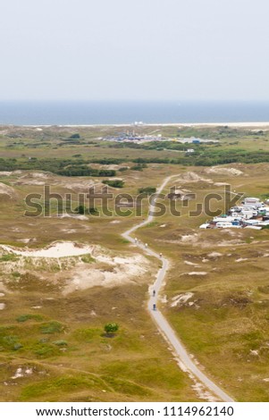 Aerial view of a footpath in between overgrown sand dunes in Norderney, Germany. The beach in the background.