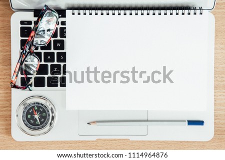 Empty page of white notebook paper with pencil, glasses and compass on laptop on wood table. Business and finance concept.