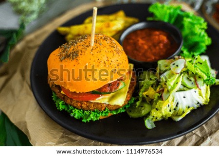 On a stylish, black plate, chicken burger, crispy bun, fresh salad, potato slices, hot sauce, tomato, cheese, radish. Kraft paper, fast food
