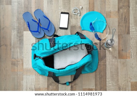 Flat lay composition with sports bag and equipment for swimming pool on wooden floor, top view