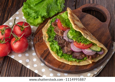 Delicious fresh homemade sandwich with roasted meat, tomato, onions and lettuce on wooden board on dark wooden table. Doner kebab. Healthy food concept.