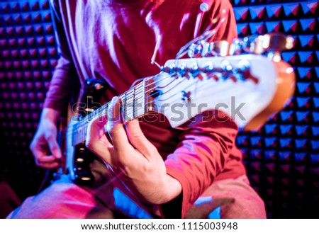 Young man playing on the guitar in sound recording studio. Modern background