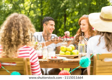 Handsome man offering fruit to his girlfriend while having a garden party with friends Royalty-Free Stock Photo #1115011664