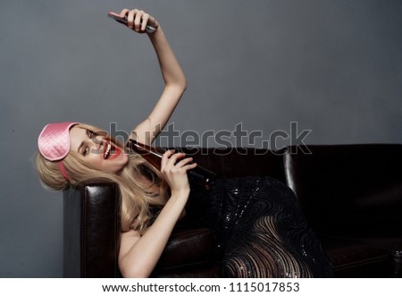   woman in the mask for the eyes lies on the couch taking pictures of herself on the weekend                             