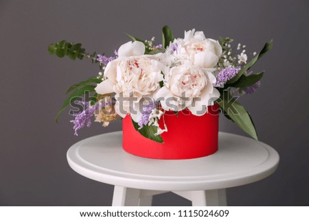 Box with beautiful peony flowers on stool against grey background
