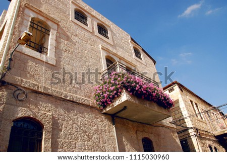 The wall of the house against the blue sky. The house is made of white stone. Balcony with flowers. Israel. Royalty-Free Stock Photo #1115030960