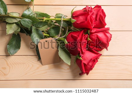 Beautiful roses with tag on wooden background