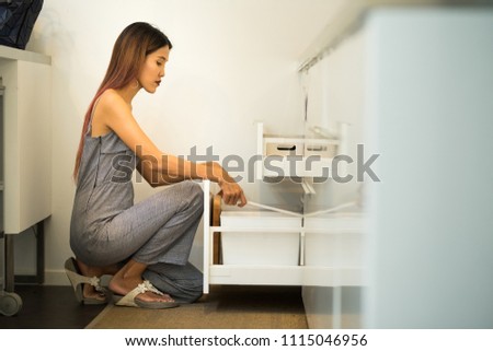 Young woman sit on knee in her kitchen open cupboard and find tools or materials