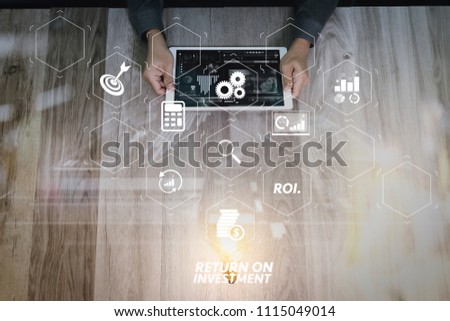 ROI Return on Investment indicator in virtual dashboard for improving business. Creative business working.  Photo graphic designer hand working with design digital tablet and ligt bulb on wood table.