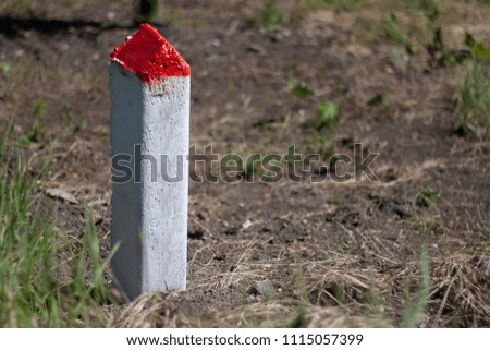 white concrete column with red top on the background of the soil and grass
