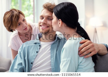 Pleasant kiss. Nice happy man smiling while being kissed by his wife