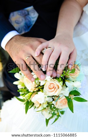 Hands of newlyweds with wedding rings on a bouquet of the bride. 