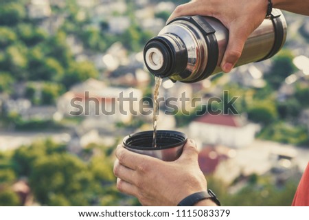Traveler man pouring tea from thermos cup, outdoors. Young man drinking tea at cup. Theme travel. Man pouring a hot drink in mug from thermos.  