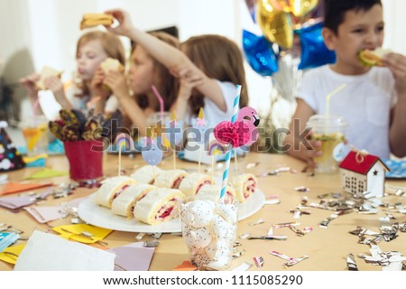 The children and birthday decorations. The boys and girls at table setting with food, cakes, drinks and party gadgets.