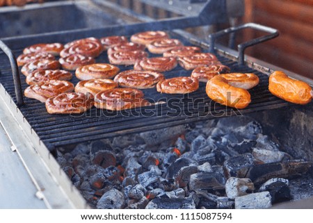 Grilled sausage on a grill with a delicious crust on the background of vegetables. Summer holidays and food in nature. Stock Photo