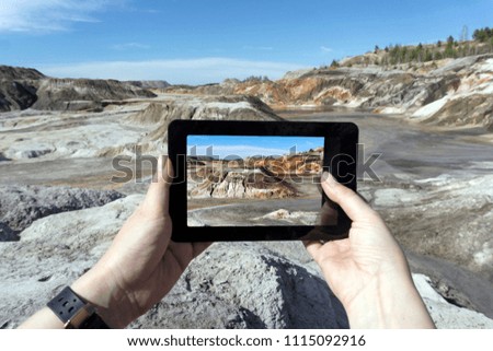 Female hands photograph with a tablet a hilly desert terrain; On the device screen, the image is better than reality