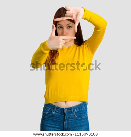 Young redhead girl with yellow sweater focusing face. Framing symbol on grey background
